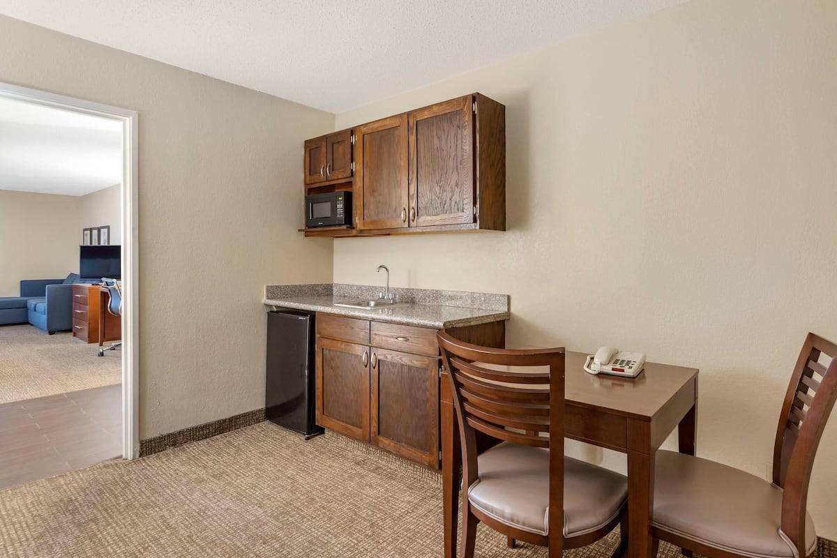 A compact kitchen with wooden cabinets, a microwave, a sink, and a dining area with a table and chairs.