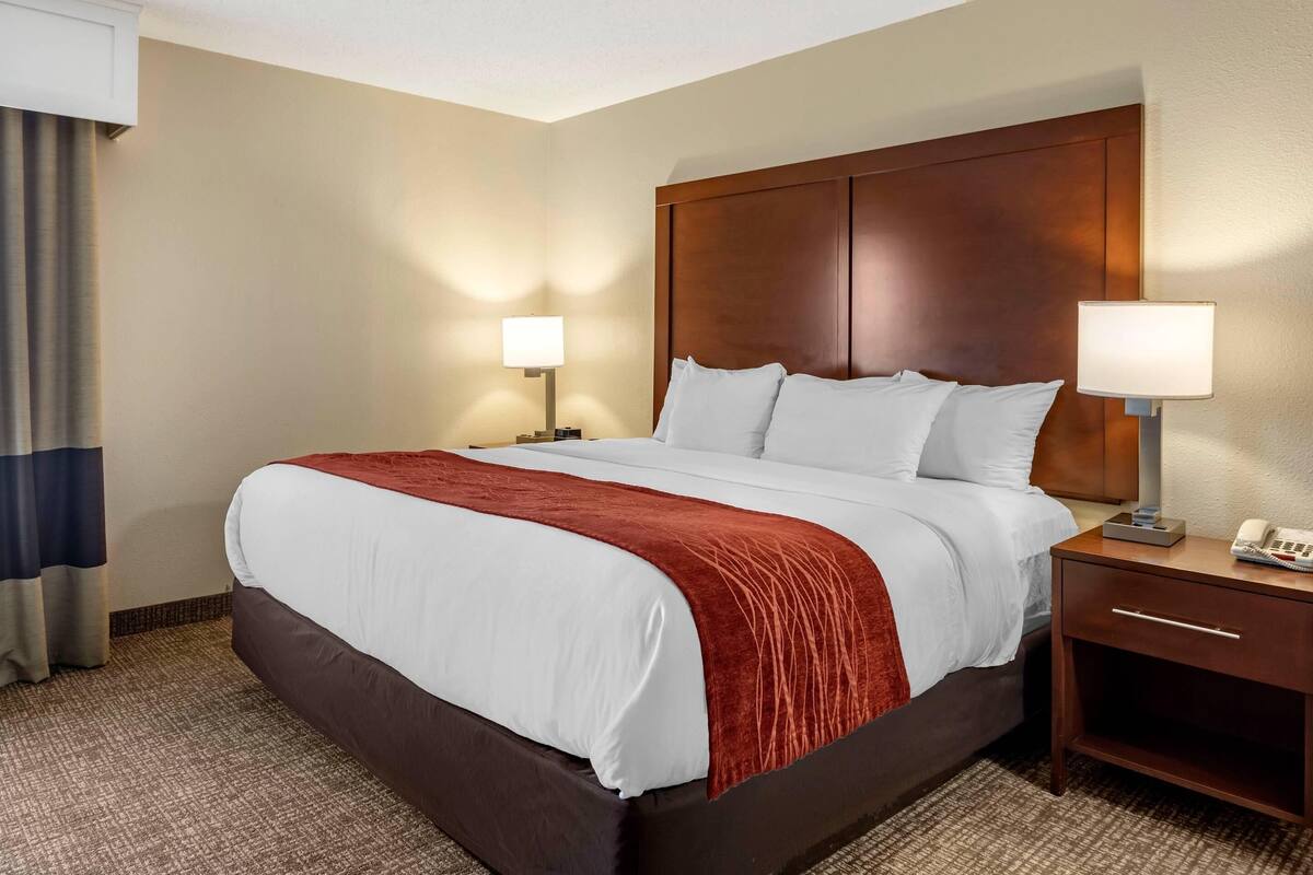 A hotel room with a large bed, a wooden headboard, two bedside tables with lamps, and a carpeted floor.