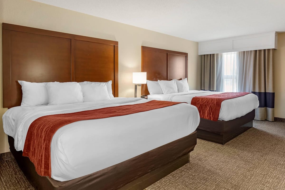 A hotel room with two beds, a large window with curtains, and a lamp.