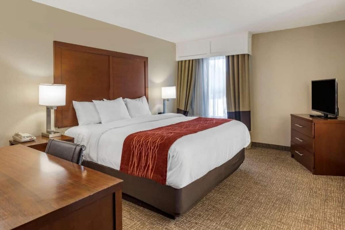 A hotel room with a bed, bedside tables, a desk, a television, and a window with curtains.