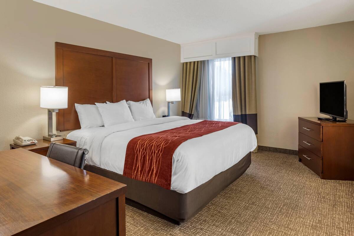 A hotel room with a bed, a desk, a television, and a window with curtains.
