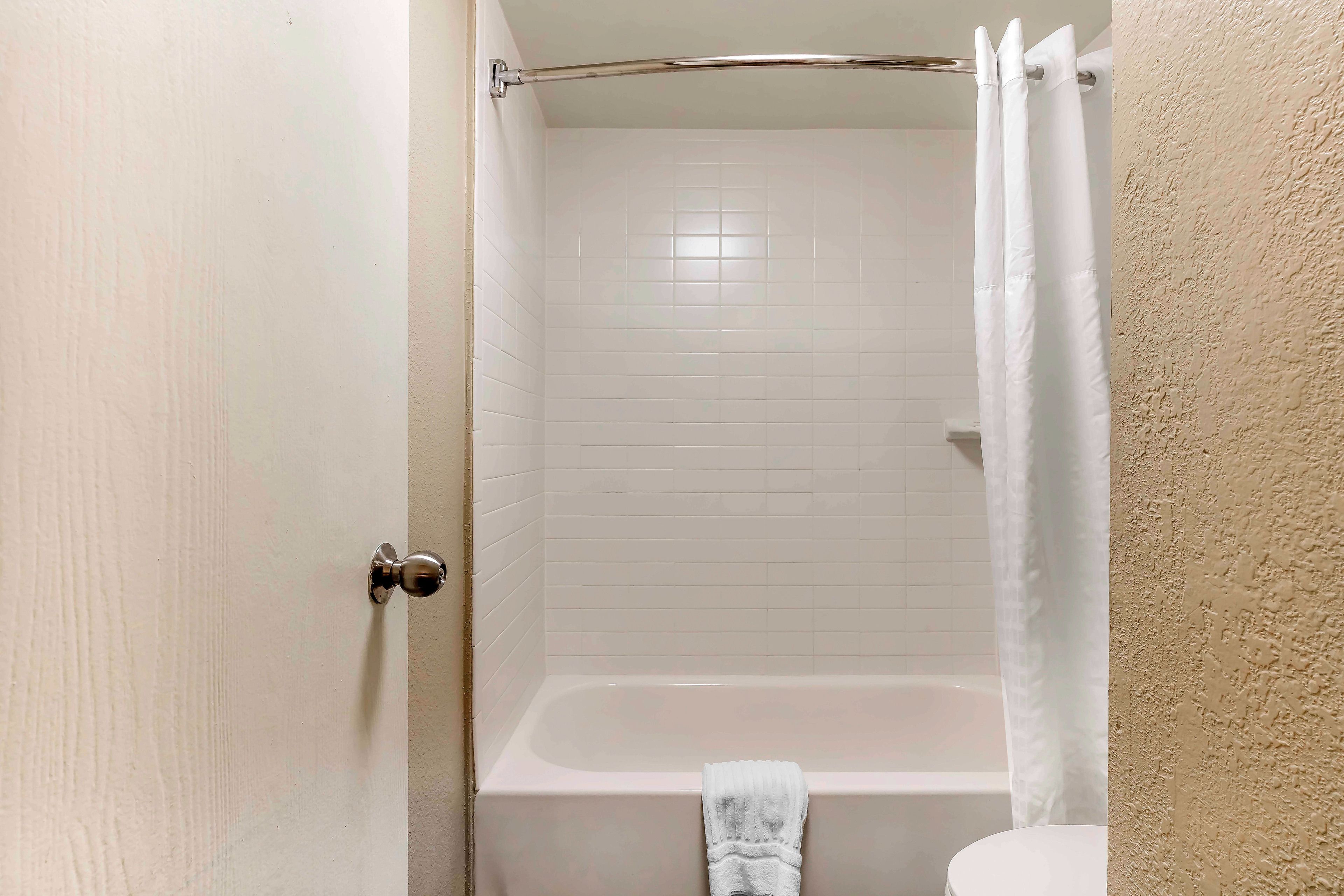 Un baño con una bañera blanca, una toalla blanca colgada en la pared y una puerta blanca.