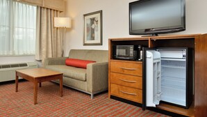 Une chambre d’hôtel équipée d’un canapé, d’une petite table en bois, d’une télévision, d’un four à micro-ondes et d’un réfrigérateur.