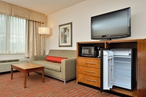 Habitación de hotel con sofá, una mesita de madera, televisión, microondas y refrigerador.