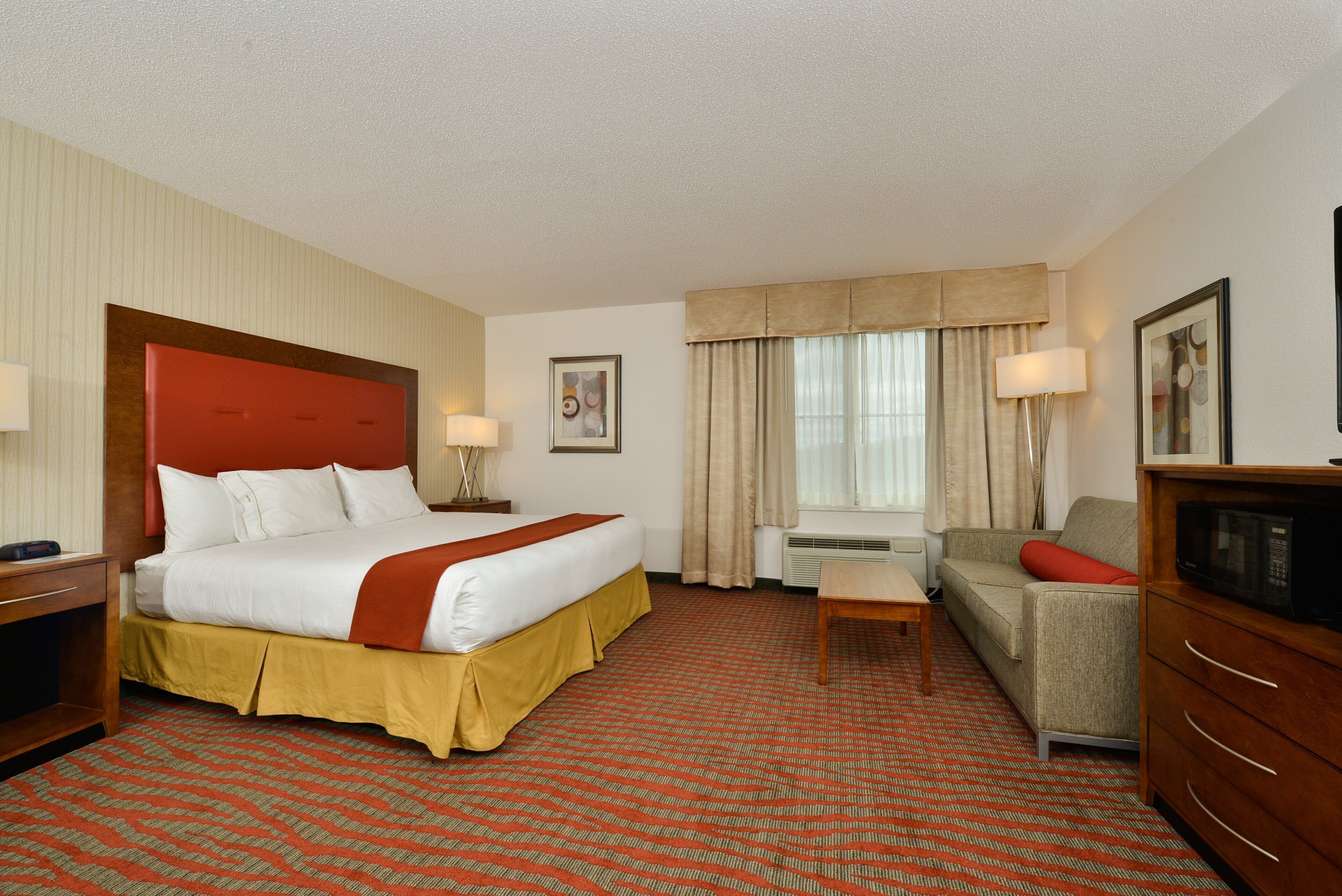 Quarto de hotel com uma cama grande, um sofá, uma mesinha e uma televisão.