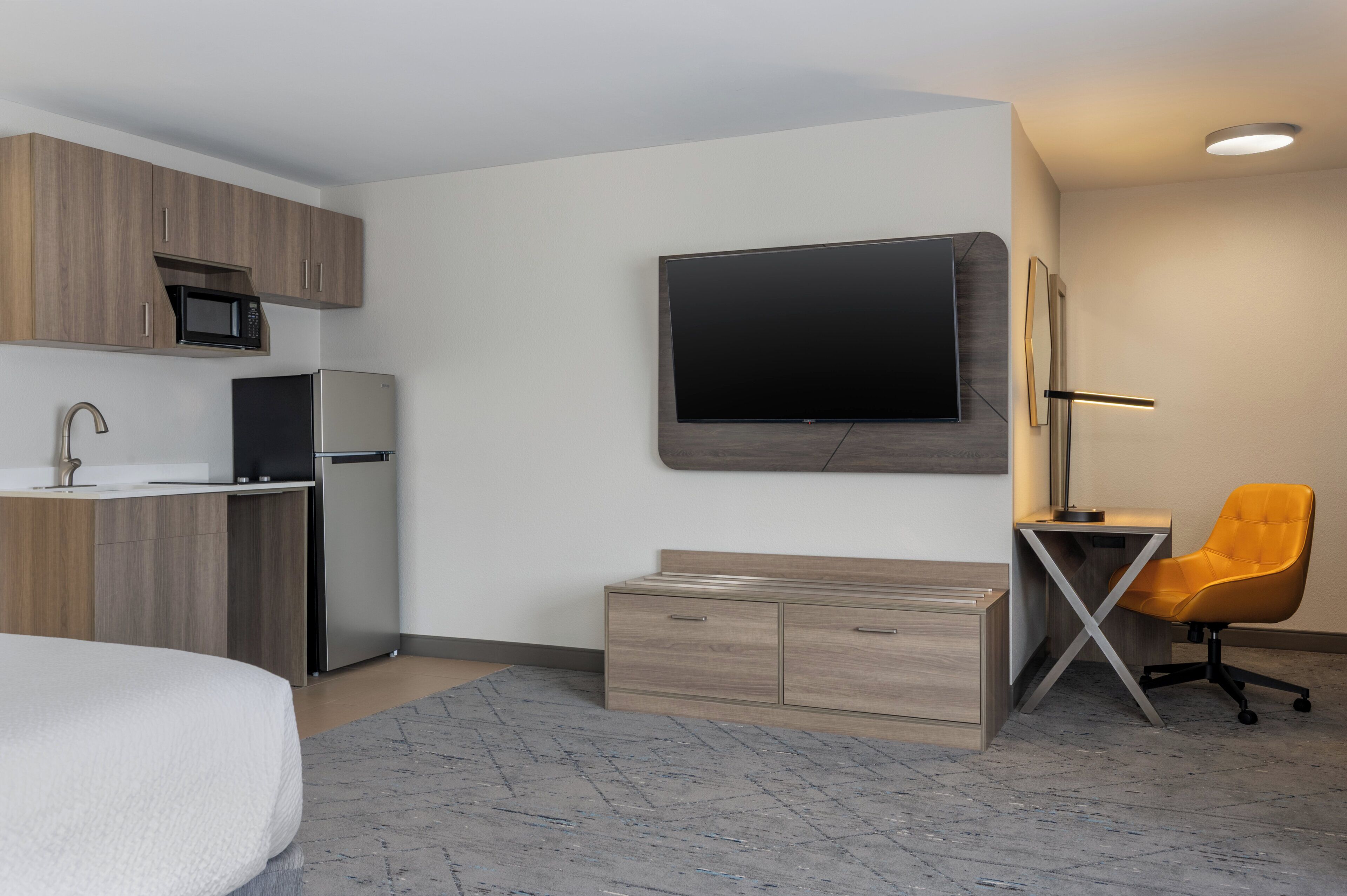 Quarto de hotel moderno com cozinha compacta, TV de tela plana, escrivaninha com cadeira e uma cama.
