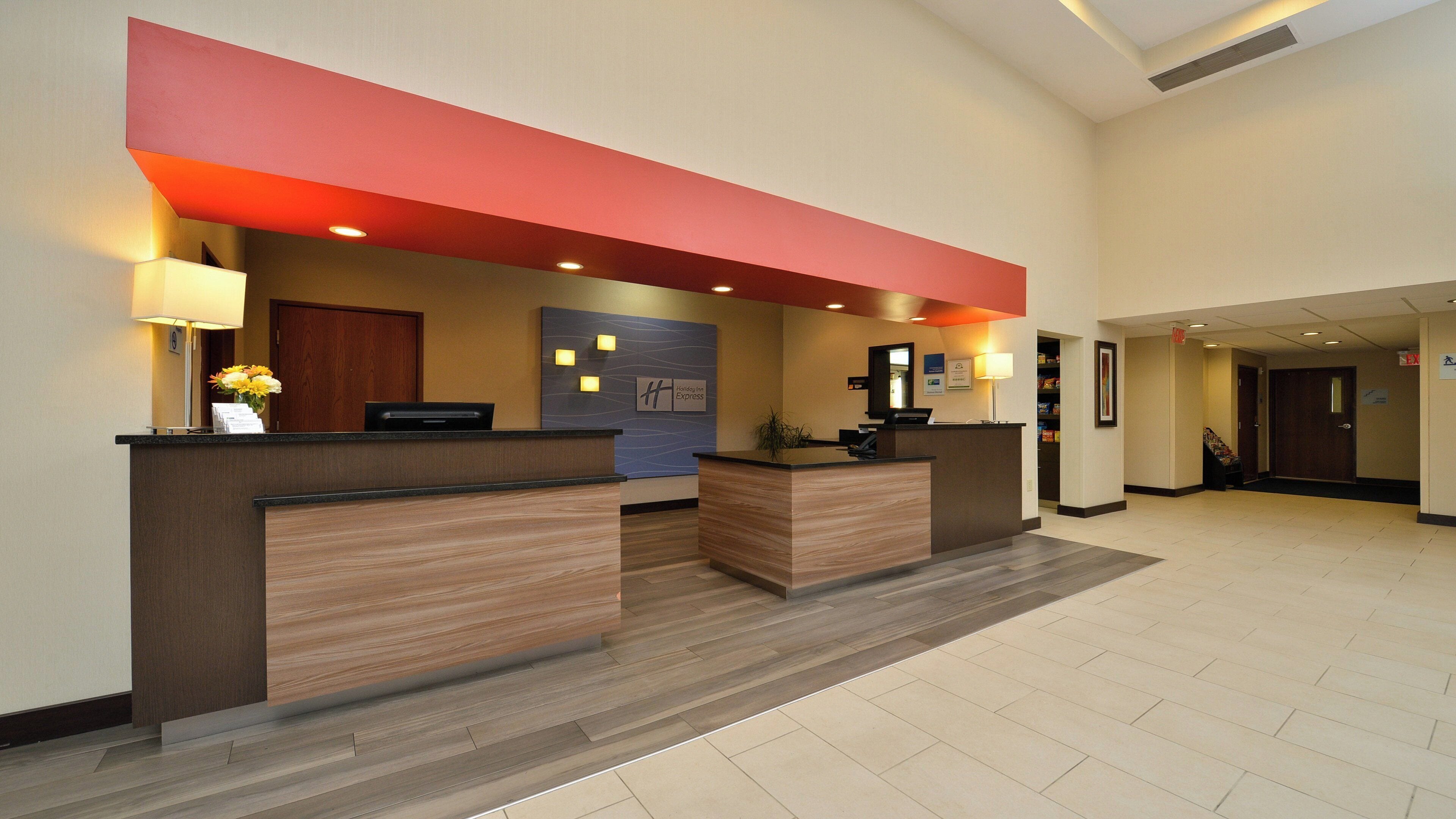 A hotel reception area with two reception desks, a wall-mounted sign for Holiday Inn Express, and a staircase leading to another floor.