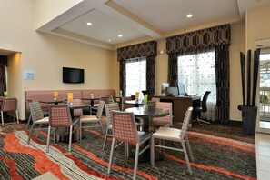 Un comedor de hotel con mesas redondas, sillas, un televisor y una alfombra estampada.