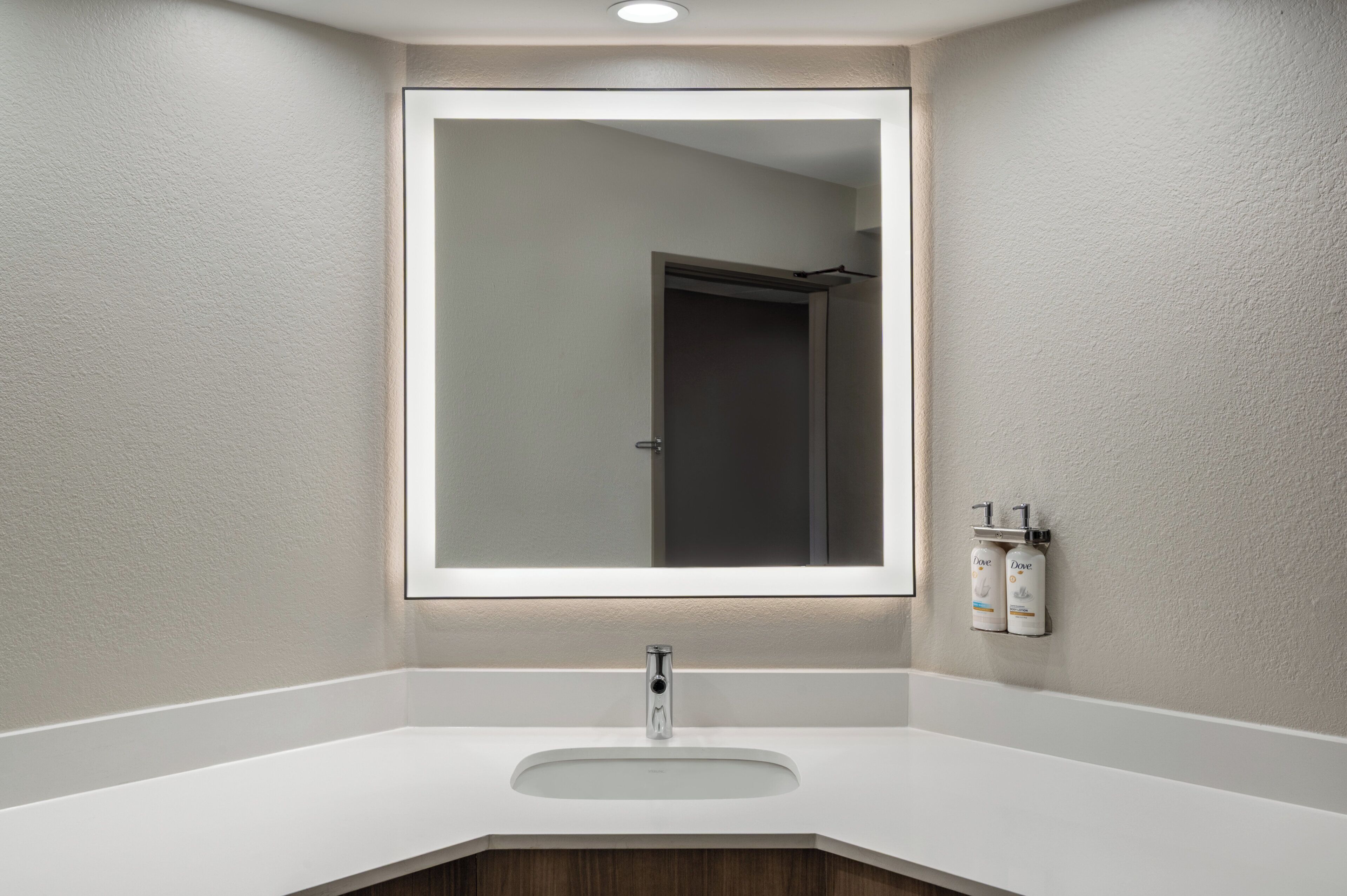A bathroom with a white sink, a large mirror, and two toiletry dispensers on the wall.