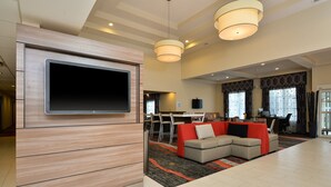 Un salon moderne avec un téléviseur à écran plat fixé sur un panneau en bois, un canapé d’angle et un coin repas à l’arrière-plan.