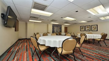 A conference room with multiple tables and chairs, a flat-screen TV mounted on the wall, and patterned carpet flooring.