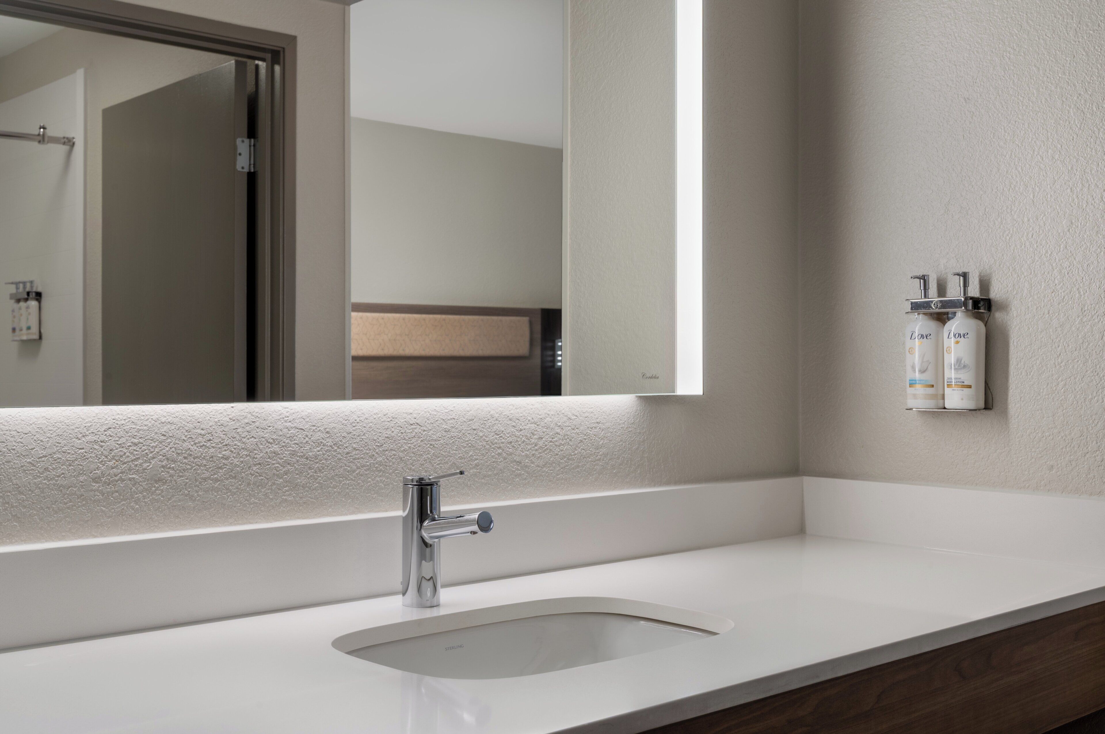 Un baño con un lavamanos blanco, un espejo y dos botellas de artículos de tocador en la pared.