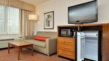 Habitación de hotel con sofá, mesa, televisión, microondas y refrigerador.