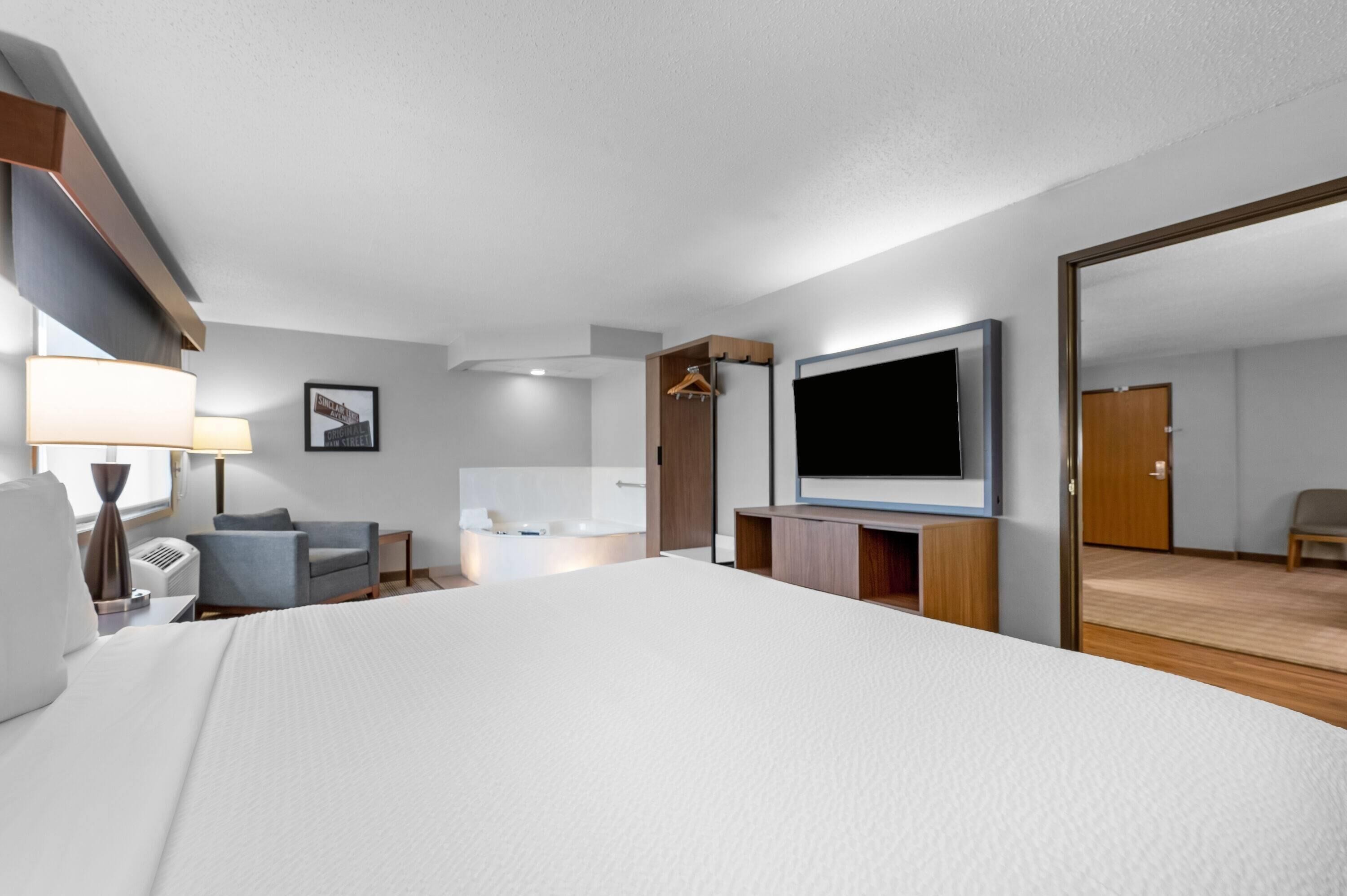 Une chambre d’hôtel avec un grand lit, un téléviseur à écran plat, un bureau avec une chaise, un canapé, une lampe et un miroir.