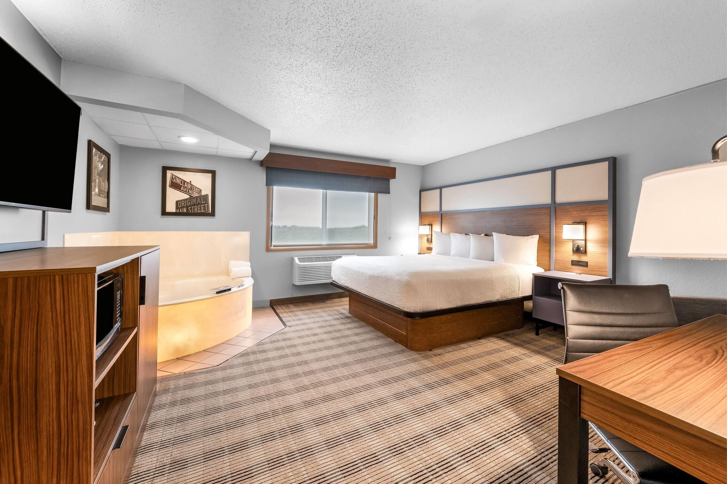 Una habitación de hotel con cama, mesita de noche, lámpara y escritorio con silla.