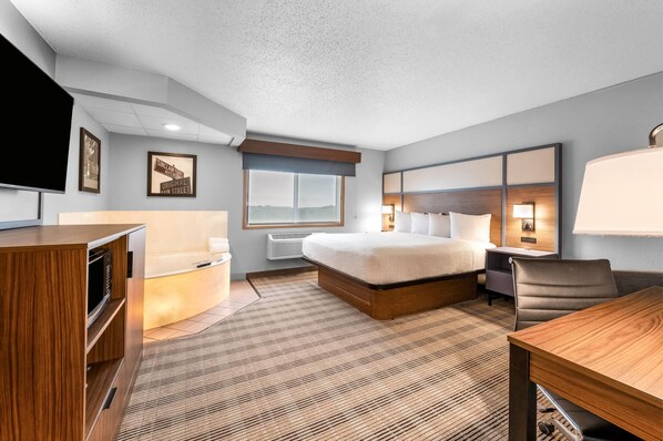 A hotel room with a bed, bedside table, lamp, and a desk with a chair.