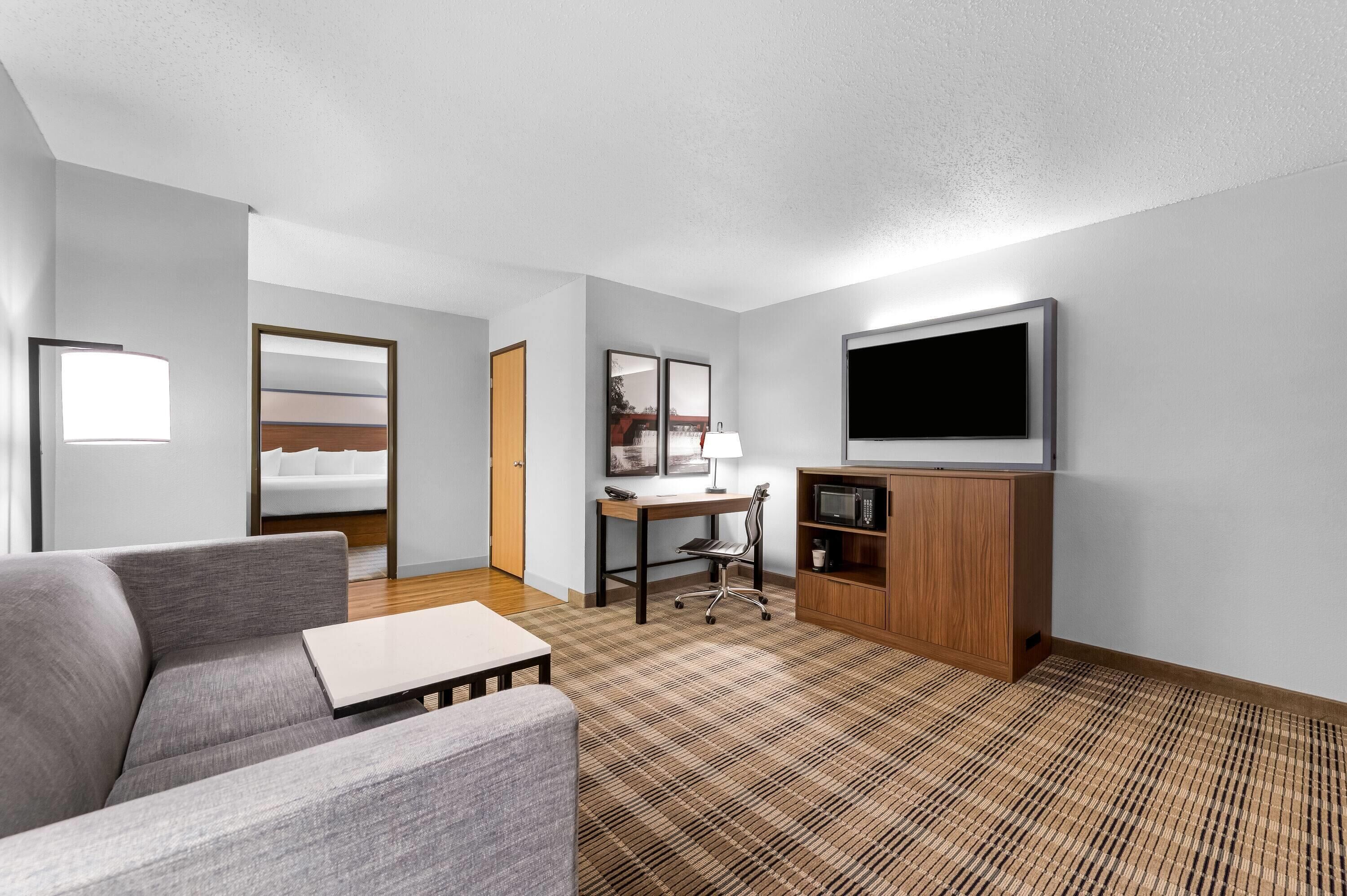 A modern hotel room with a sofa, a desk with a lamp, a television, and a microwave.