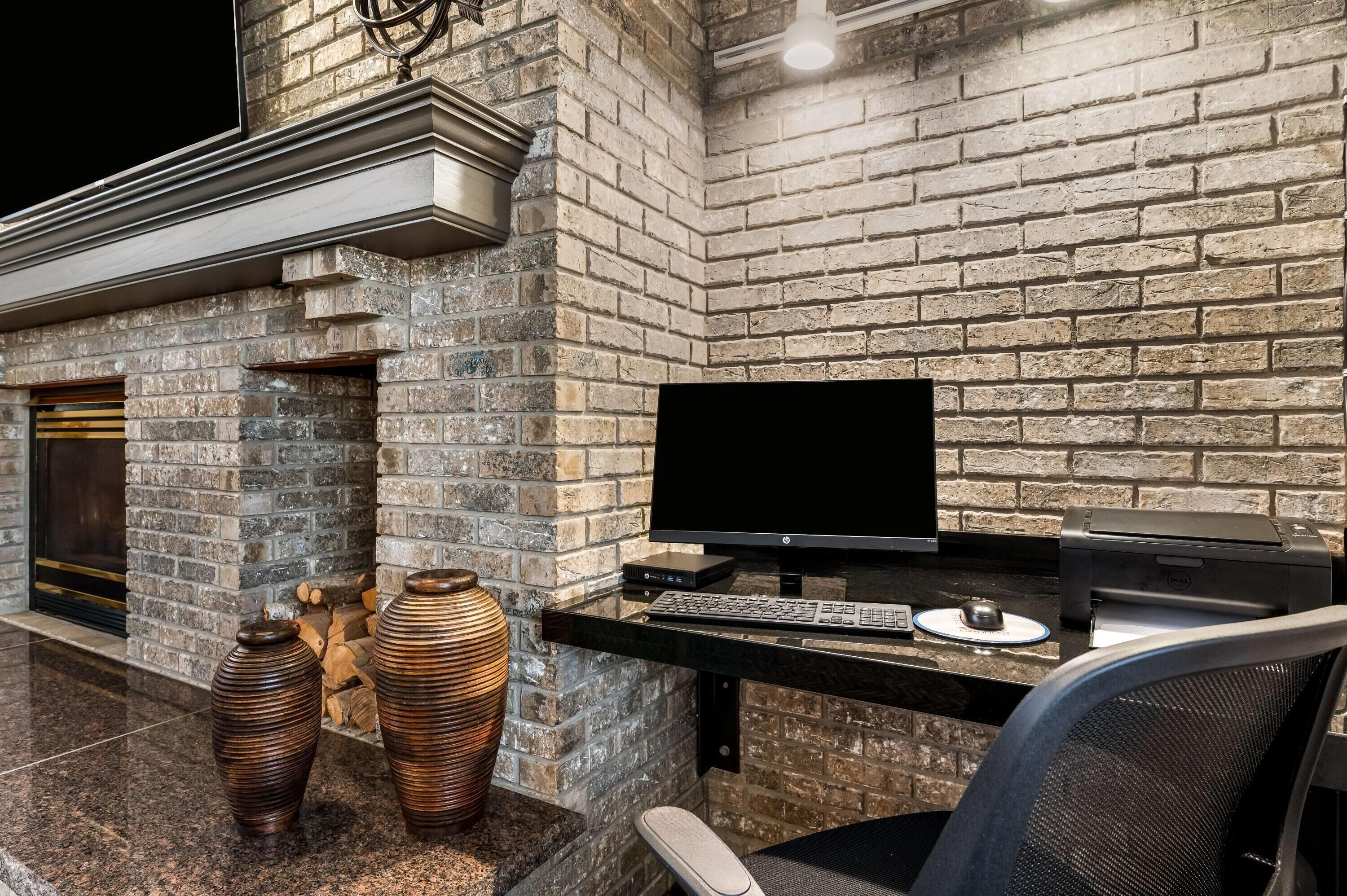 A modern workspace with a brick wall, a fireplace, and a computer setup.