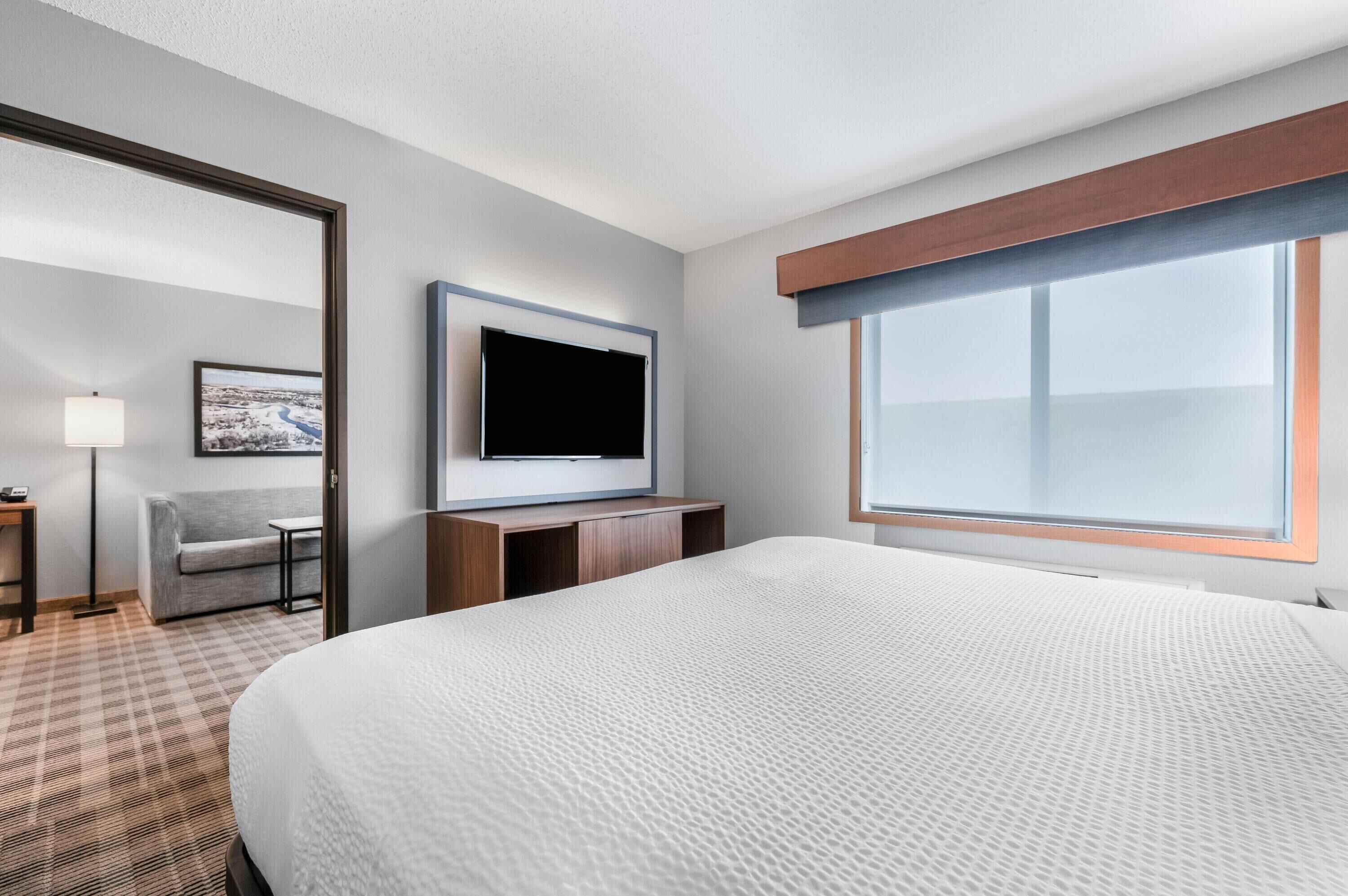 Ein Hotelzimmer mit einem Bett, einem an der Wand montierten Fernseher, einem Schreibtisch, einem Stuhl und einem Fenster.