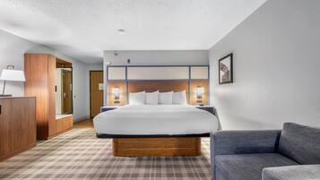 A hotel room with a large bed, a wooden headboard, a nightstand, a desk, a lamp, a couch, and a patterned carpet.