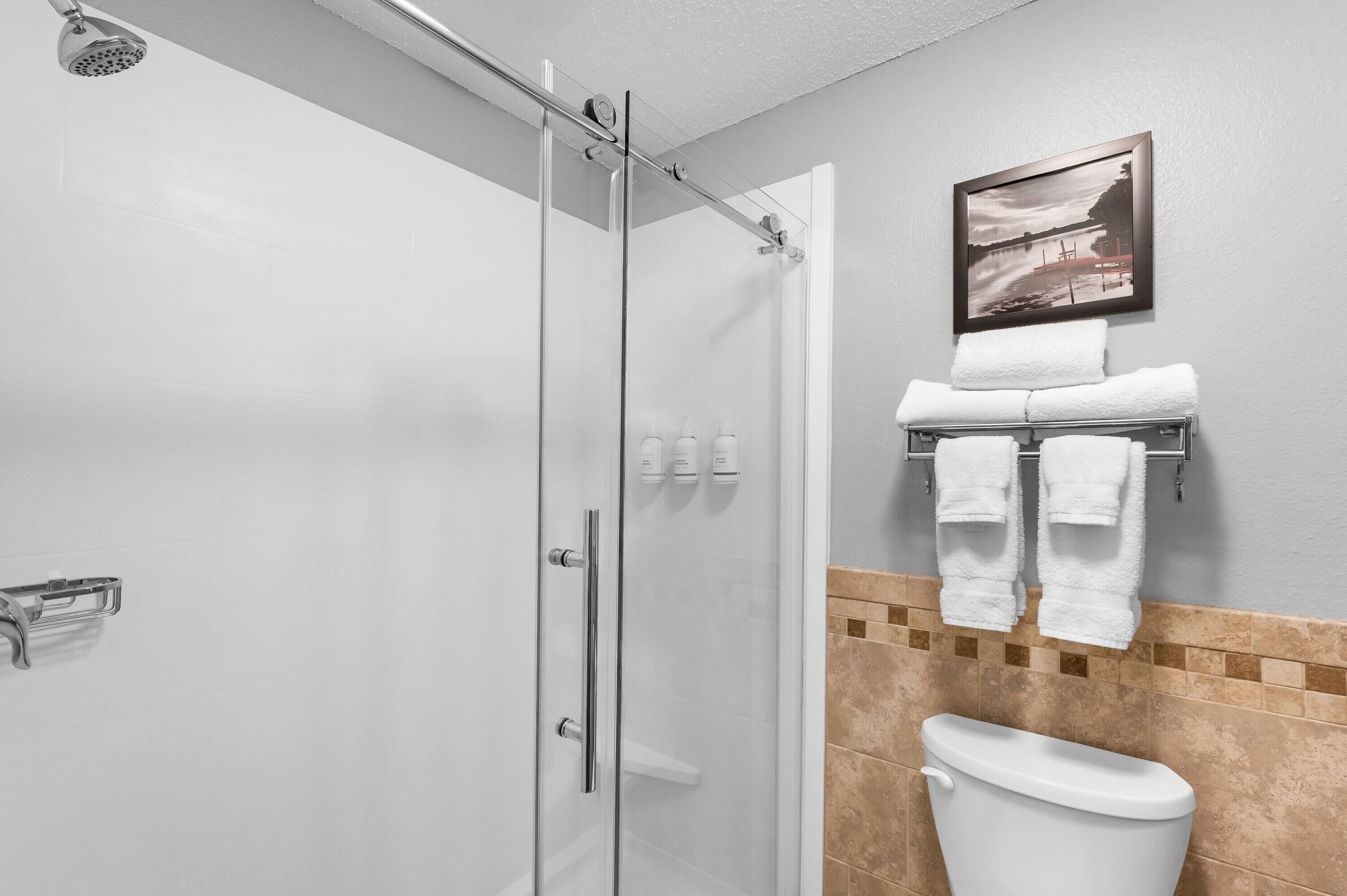 A modern bathroom with a glass shower enclosure, a toilet, and a towel rack with towels.