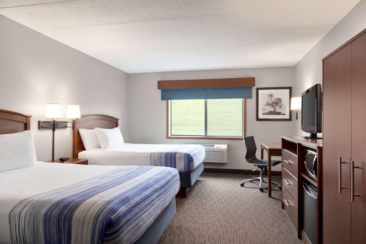A hotel room with two beds, a desk, a chair, a television, and a window with a view of the outdoors.