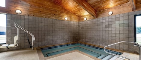 Ein Wellnessbereich mit Holzboden, gefliesten Wänden, einem Pool und einer barrierefreien Sitzbank.