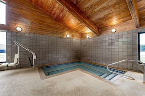 A spa area with a wooden ceiling, tiled walls, a pool, and a wheelchair-accessible bench.