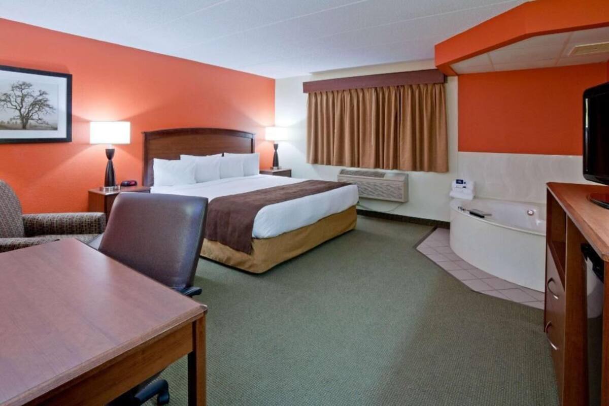Une chambre d’hôtel équipée d’un lit, d’un bureau, d’une chaise, d’une télévision, d’une fenêtre avec des rideaux et d’un climatiseur fixé au mur.