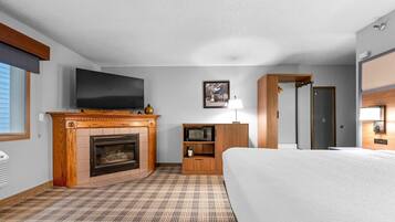 A hotel room with a fireplace, a television, a microwave, a bed, and a door.