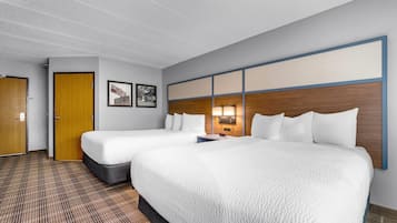 A hotel room with two beds, a wooden door, a wall-mounted lamp, and a check-in desk.