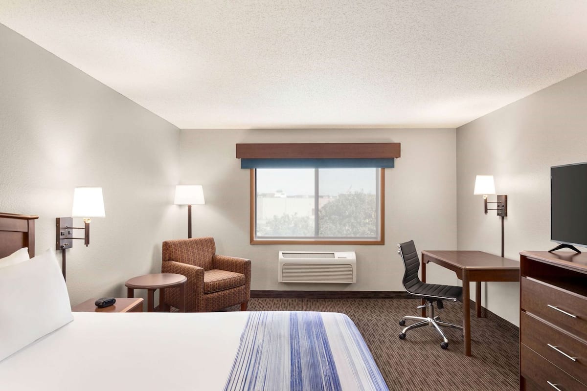 A hotel room with a bed, a desk, a chair, a small table, a lamp, a TV, and a window with a view.