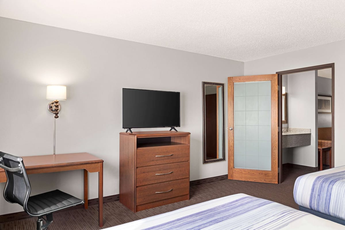 A hotel room with a wooden desk, a television, a wardrobe, a mirror, and a bed.