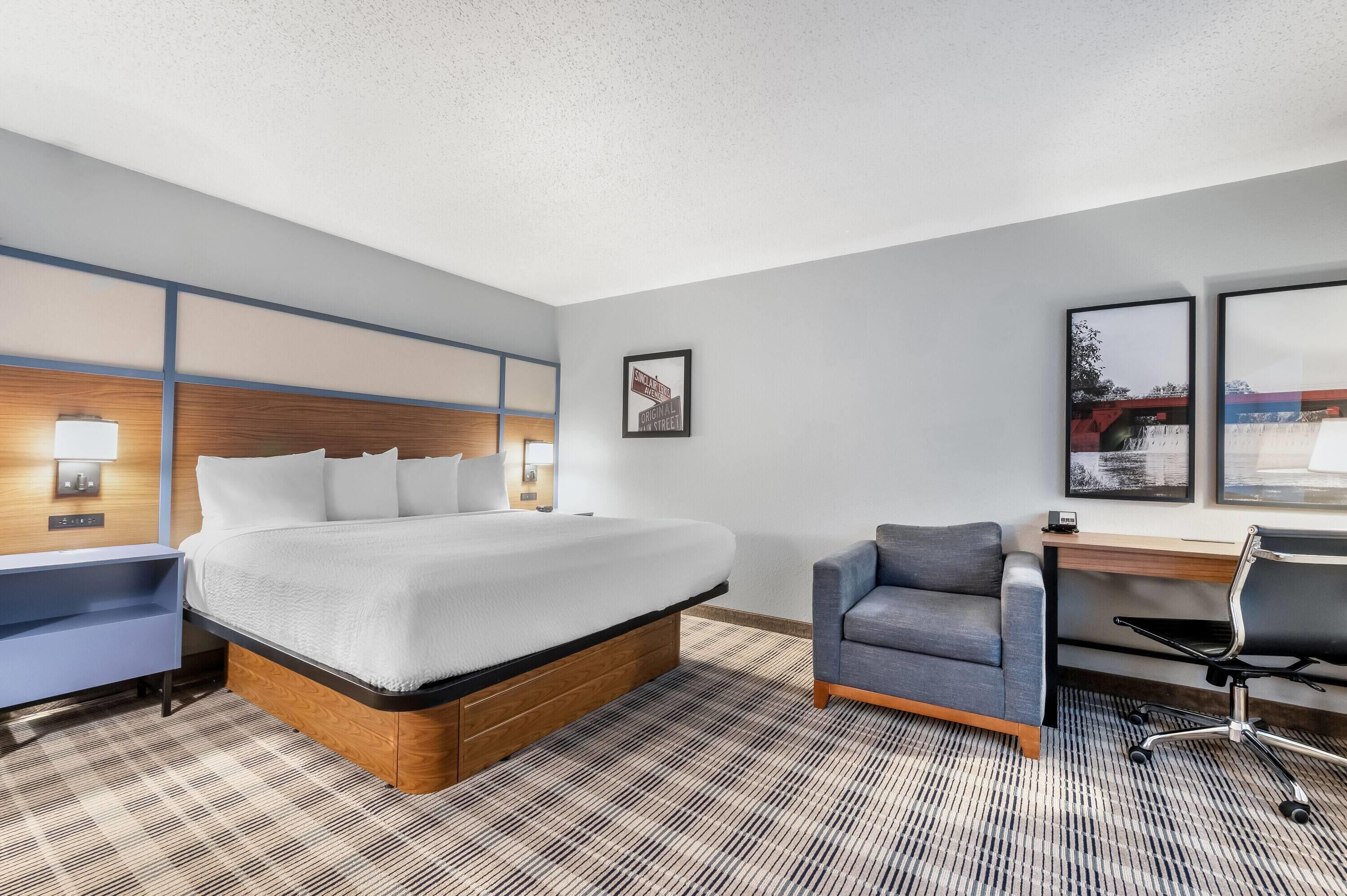 Habitación de hotel con una cama grande, un escritorio, una silla y vistas al exterior.