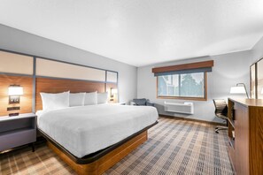 Une chambre d’hôtel avec un grand lit, un bureau, une chaise, une fenêtre et un climatiseur fixé au mur.