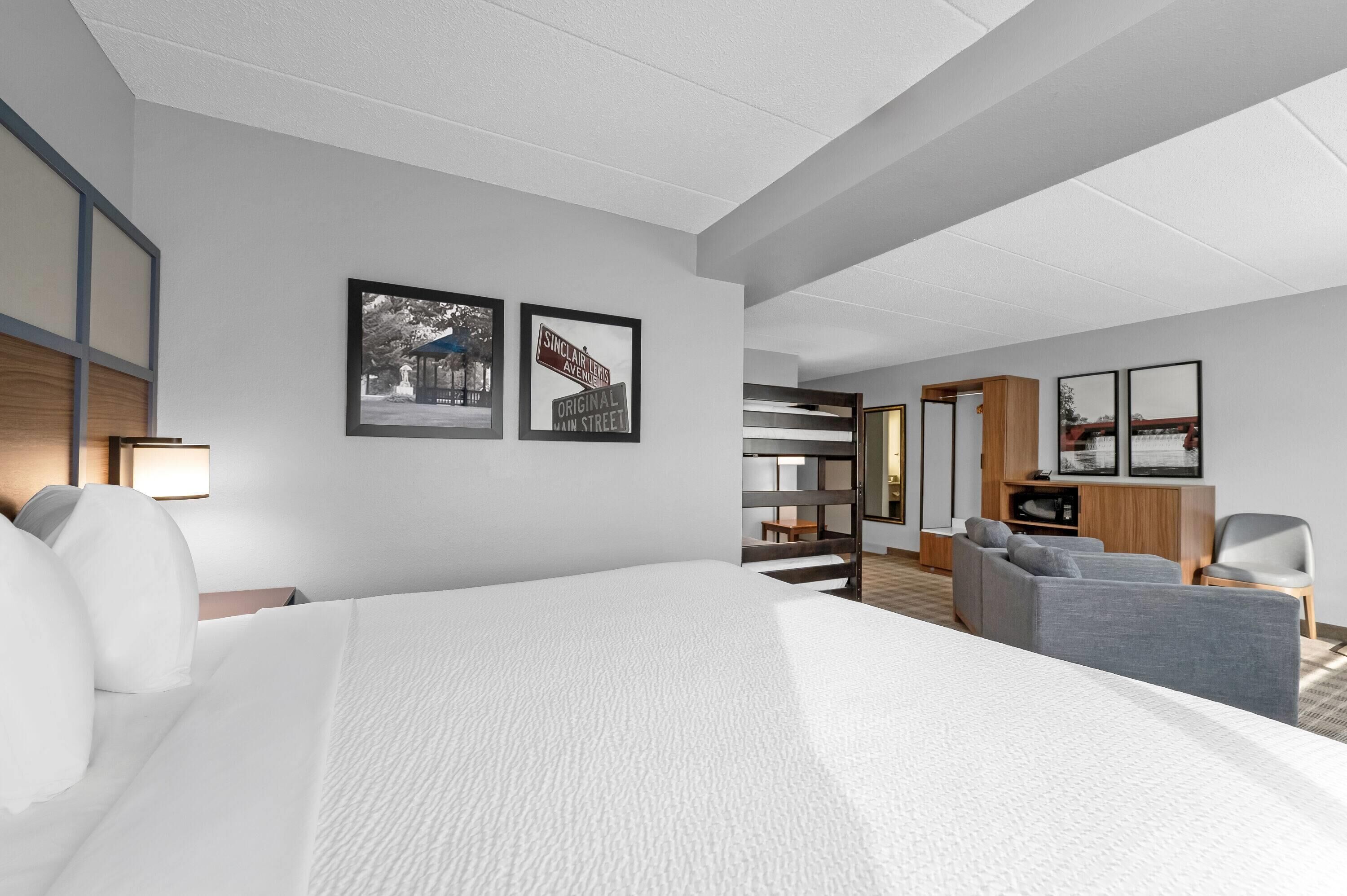 Una habitación de hotel con una cama grande, una zona de estar con sofá y sillones, un televisor y cuadros en la pared.