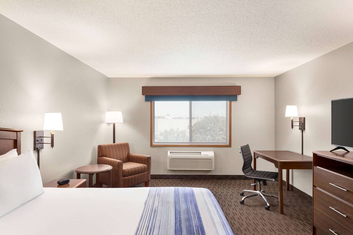 A hotel room with a bed, two chairs, a desk, a TV, and a window with a view.
