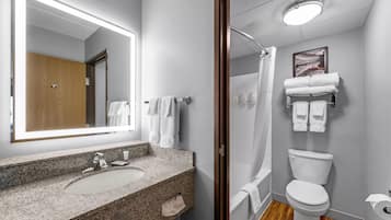 Un baño moderno con lavamanos de granito, inodoro, ducha y un espejo grande.