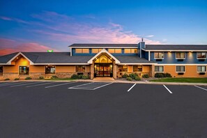A hotel with a main entrance, a parking lot, and a clear sky.