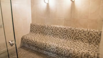 Un área de ducha con puerta de cristal, paredes con azulejos y un banco con diseño de mosaico.