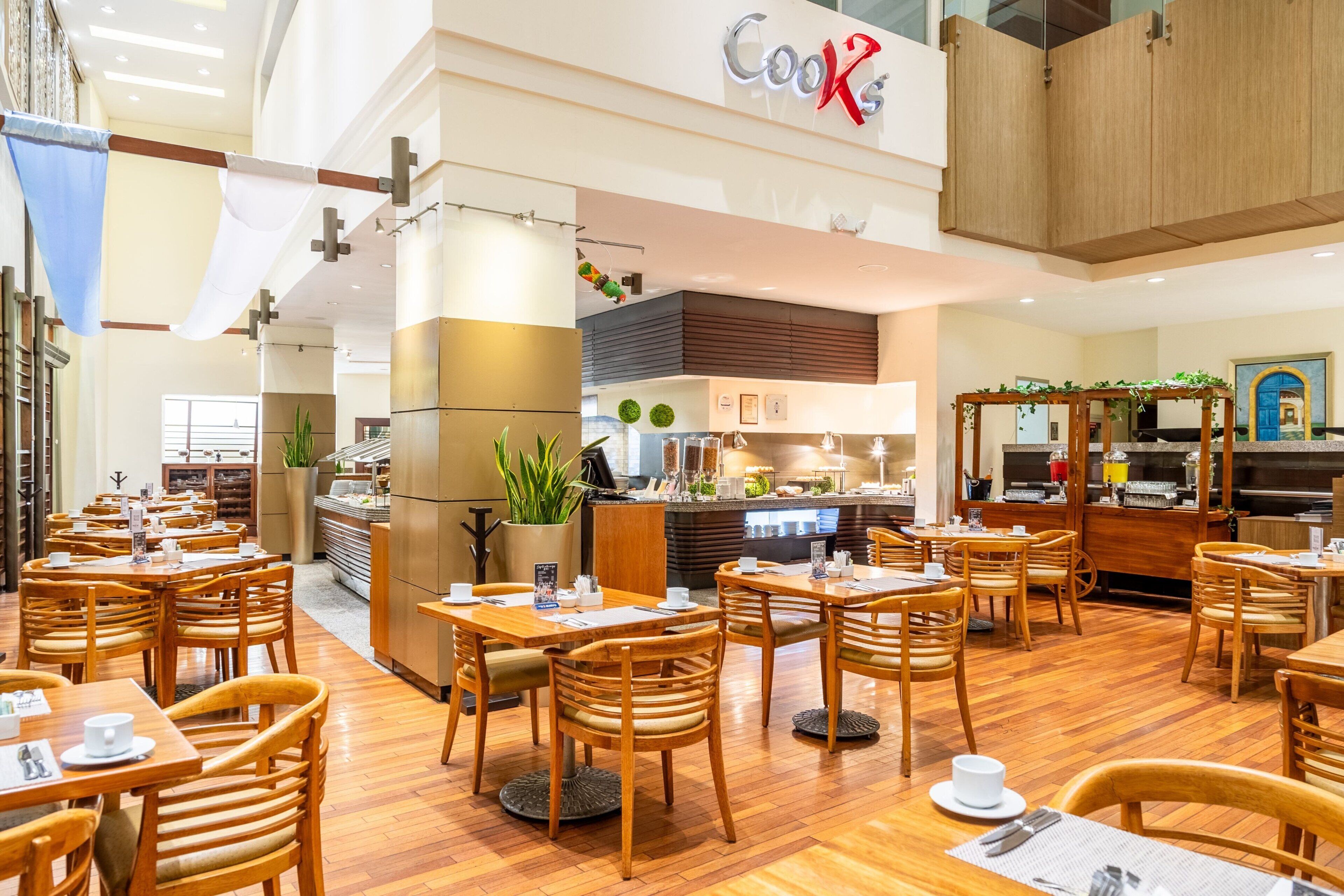 Un restaurante con mesas y sillas de madera, una zona de cocina y un letrero que dice "Cooks".