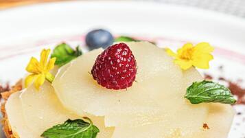 Ein Dessert mit säuerlichem Untergrund, bedeckt mit einer cremigen Schicht, einer Himbeere und verziert mit Minzblättern und gelben Blüten.