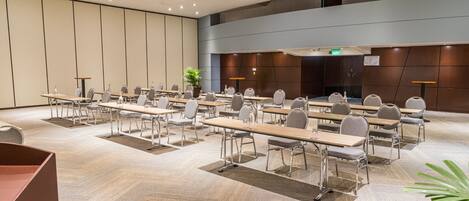 Un salón de conferencias con varias mesas y sillas, una planta grande y un diseño moderno.