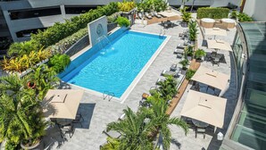 Une piscine sur le toit, agrémentée de chaises longues et de parasols, entourée de verdure, avec un parking à plusieurs niveaux en arrière-plan.