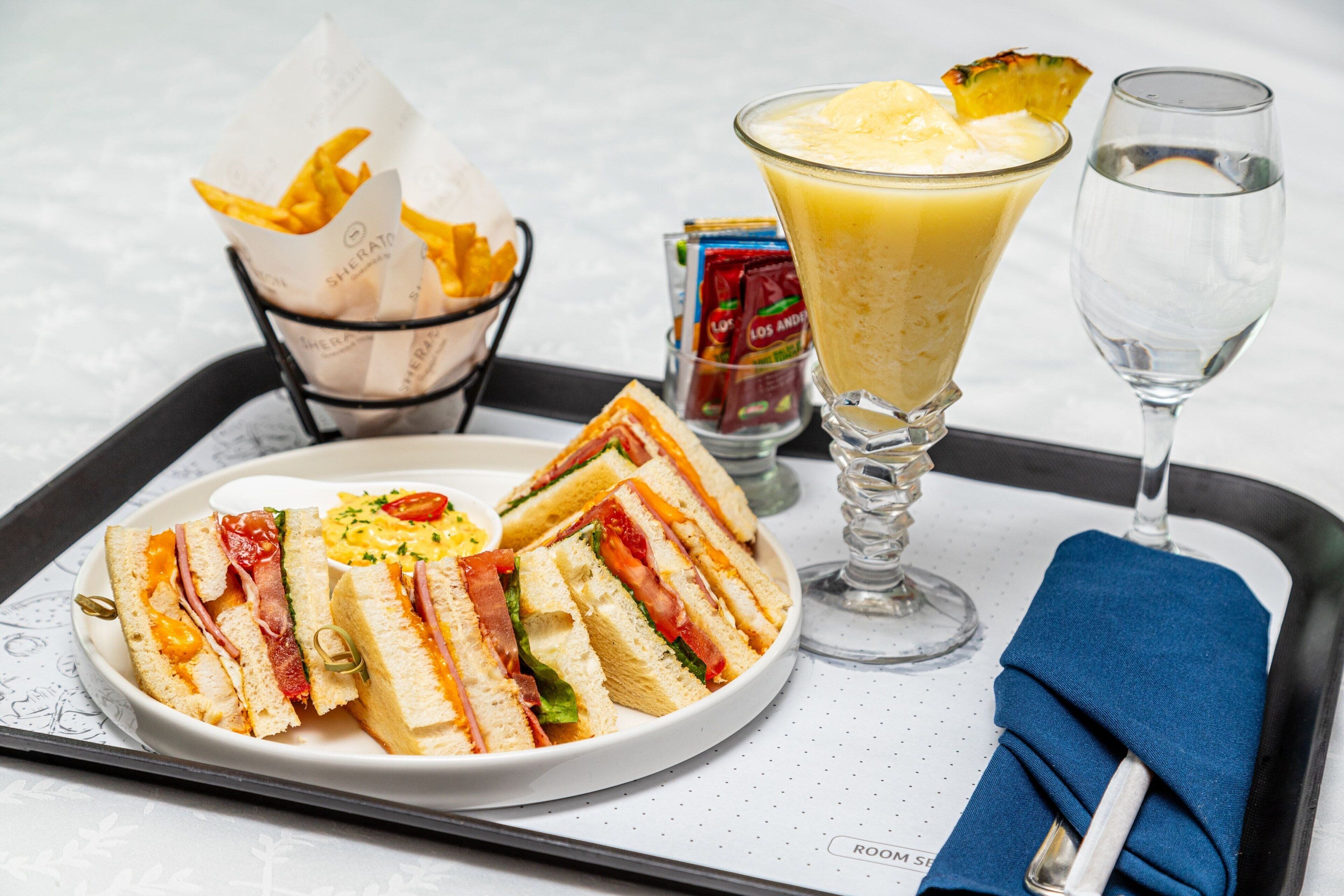 Una bandeja con sándwiches, un vaso de zumo de naranja y un vaso de agua.