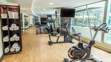 A modern gym with cardio machines, a mirrored wall, and a view of the city.