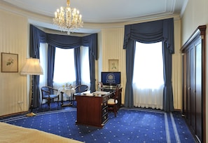 Habitación de hotel con un escritorio grande, dos sillas, una araña y una televisión.