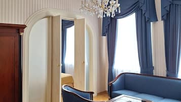 Une pièce dotée d’un lustre, de meubles recouverts d’un tissu bleu, d’un tapis à motifs et d’une armoire en bois.