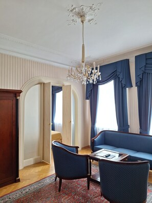 A room with a chandelier, blue upholstered furniture, a patterned rug, and a wooden cabinet.