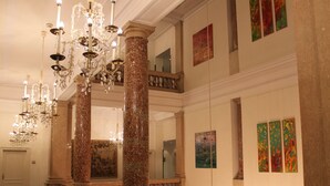 A grand lobby with marble columns, a chandelier, and artwork on the walls.